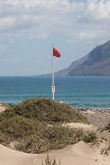 Image showing The red flag weighs in the wind at Surfers Beach Famara on Lanza