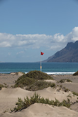 Image showing The red flag weighs in the wind at Surfers Beach Famara on Lanza