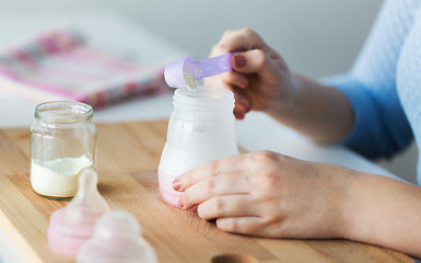 Image showing hands with bottle and scoop making formula milk