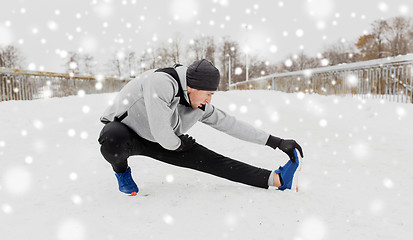 Image showing man exercising and stretching leg on winter bridge