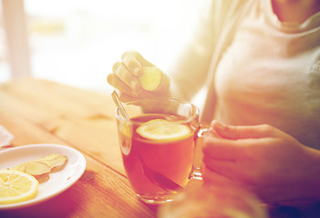 Image showing close up of woman adding ginger to tea with lemon