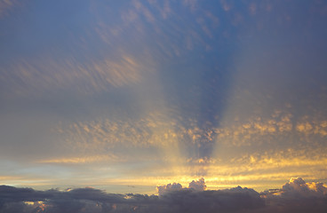 Image showing Golden sun rays from behind clouds stretch across the sky above