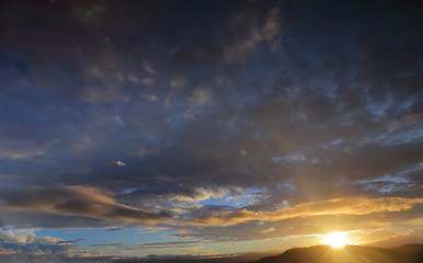 Image showing Sun setting sunburst behind mountain with blue sky and clouds ti