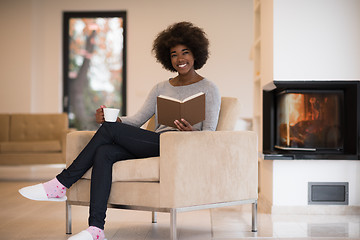 Image showing black woman reading book  in front of fireplace