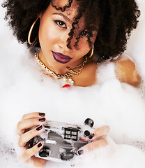 Image showing young afro-american teen girl laying in bath with foam, wearing 