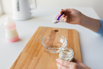 Image showing hands with spoon and jar making baby cereal