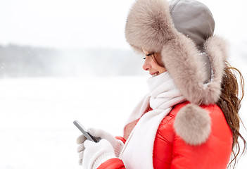 Image showing happy woman in winter fur hat with smartphone