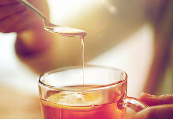 Image showing close up of woman adding honey to tea with lemon