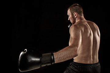 Image showing The young man kickboxing on black