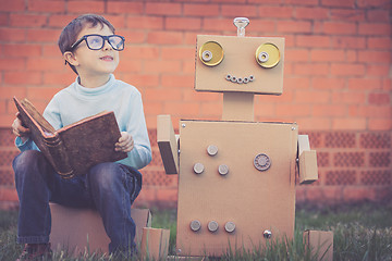 Image showing One little boy reading to  robot from cardboard boxes outdoors. 