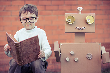 Image showing One little boy reading to  robot from cardboard boxes outdoors.