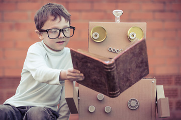 Image showing One little boy reading to  robot from cardboard boxes outdoors.