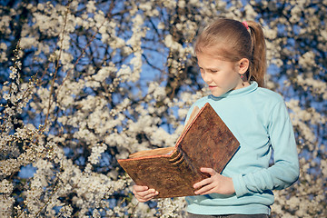 Image showing One little girl reading a book on a blossom tree.