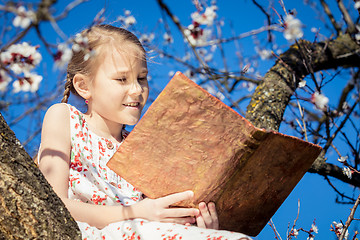 Image showing One little girl reading a book on a blossom tree.