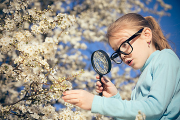 Image showing Happy little girl exploring nature with magnifying glass at the 