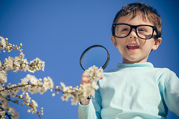 Image showing Happy little boy exploring nature with magnifying glass at the d