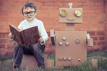 Image showing One little boy reading to  robot from cardboard boxes outdoors.