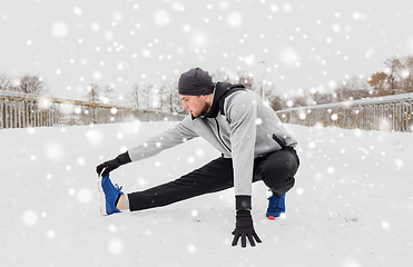 Image showing man exercising and stretching leg on winter bridge