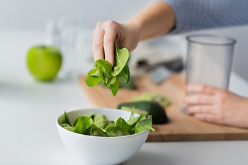 Image showing close up of woman hand adding spinach to bowl