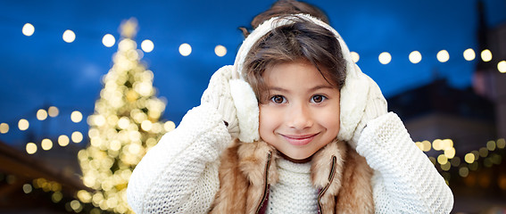 Image showing happy girl wearing earmuffs over christmas lights