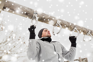 Image showing young man exercising on horizontal bar in winter