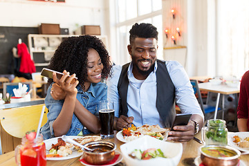 Image showing happy man and woman with smartphones at restaurant