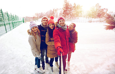 Image showing happy friends with smartphone on ice skating rink