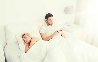 Image showing man texting message while woman is sleeping in bed