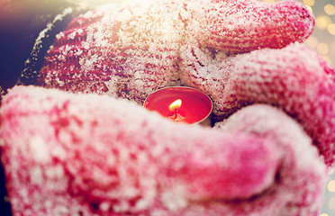 Image showing close up of hands in winter mittens holding candle