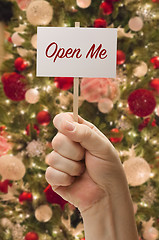Image showing Hand Holding Open Me Card In Front of Decorated Christmas Tree.