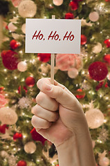 Image showing Hand Holding Ho Ho Ho Card In Front of Decorated Christmas Tree.