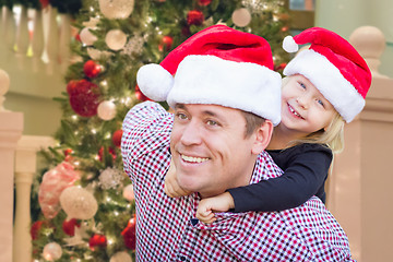 Image showing Father and Daughter Wearing Santa Hats In Front of Decorated Chr