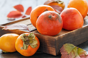 Image showing Orange persimmon and autumn leaves on wooden box.