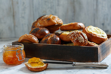 Image showing Wooden tray with buns and a jar of orange jam.