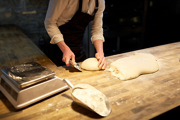 Image showing baker portioning dough with bench cutter at bakery