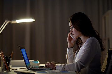 Image showing woman with laptop calling on smartphone at office