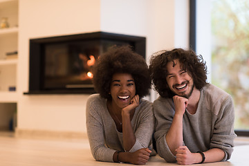 Image showing multiethnic couple lying on the floor  in front of fireplace