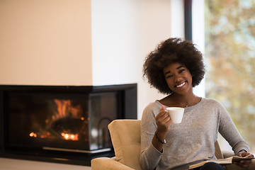 Image showing black woman reading book  in front of fireplace