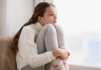 Image showing sad girl sitting on sill at home window in winter