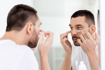 Image showing young man applying cream to face at bathroom