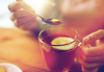 Image showing close up of woman adding honey to tea with lemon