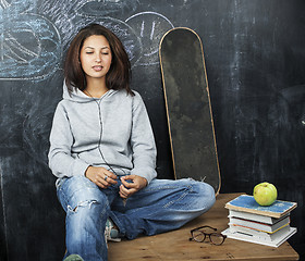 Image showing young cute teenage girl in classroom at blackboard seating on table smiling, modern pupil hipster concept, lifestyle people