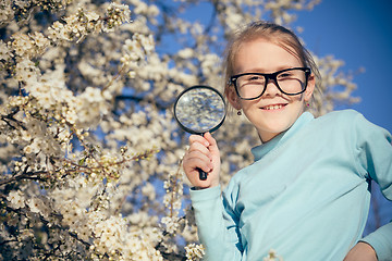 Image showing Happy little girl exploring nature with magnifying glass at the 