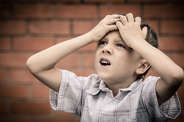 Image showing portrait one sad little boy standing near a wall  at the day tim