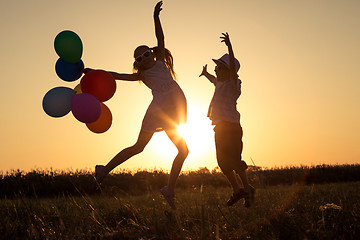 Image showing Silhouette of two happy children which playing on the field at t