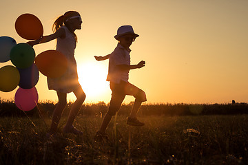 Image showing Silhouette of two happy children which playing on the field at t