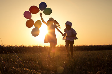 Image showing Silhouette of two happy children which playing on the field at t