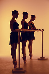 Image showing Composition from silhouettes of three young dancers in ballet poses on a orange background.