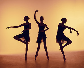 Image showing Composition from silhouettes of three young dancers in ballet poses on a orange background.