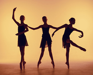 Image showing Composition from silhouettes of three young dancers in ballet poses on a orange background.